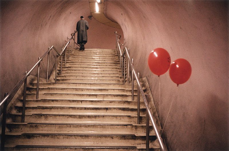 Fotografia tratta dal libro Underground di Marco Pesaresi: un pendolare sale le scale della metropolitana di King's Cross a Londra, di fianco a due palloncini rossi.