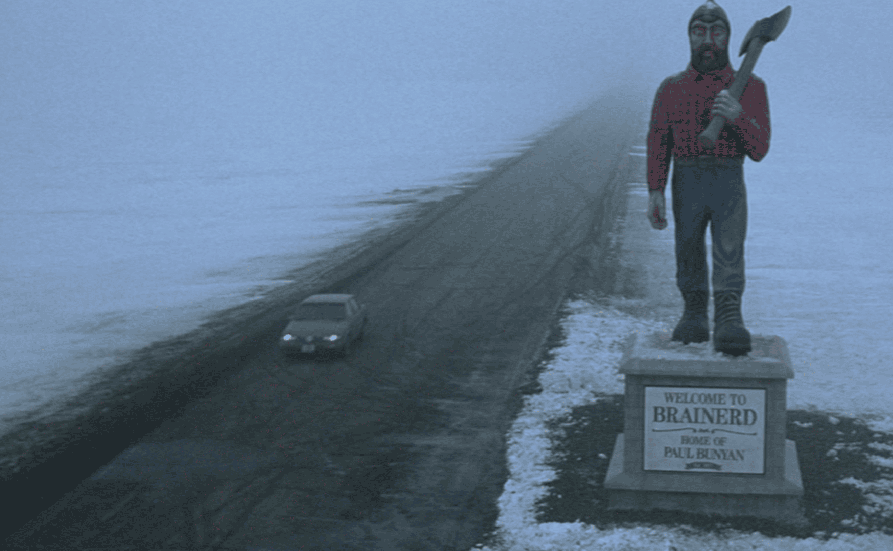A still from the movie *Fargo* showing a snow-covered landscape, a road, and a giant statue